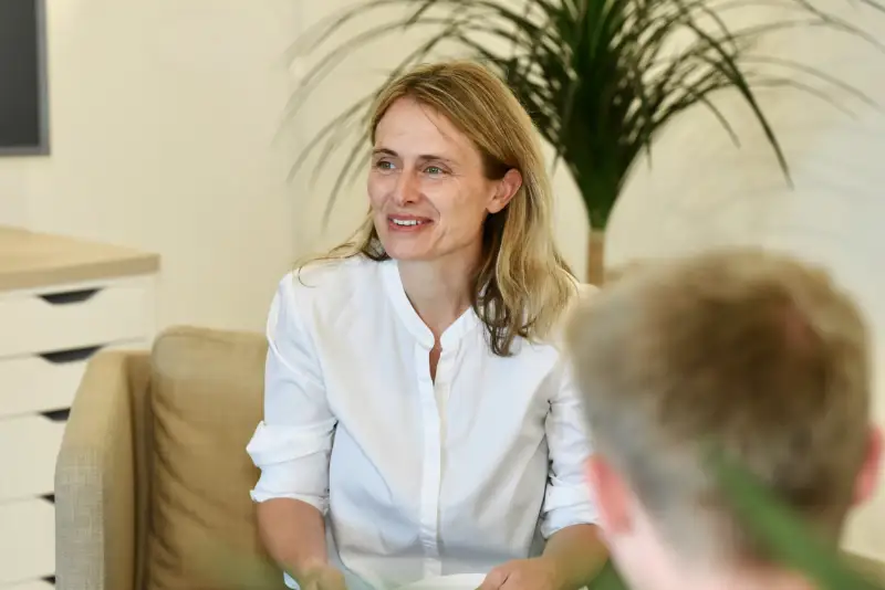 Nicole Tepaße von Rede Klartext Alt-Tag Vorschlag:  Coachin im Gespräch mit Klient im Coachingraum, sitzt entspannt auf dem Sofa, im Hintergrund eine große Zimmerpflanze