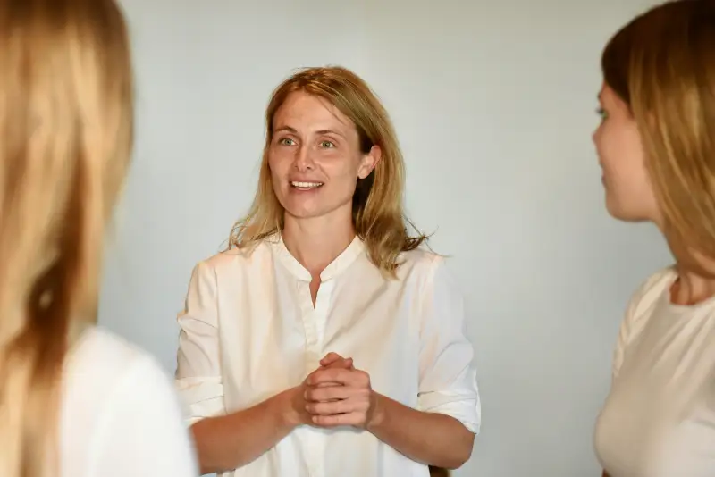 Klar, angepasst in weiblicher Form:  Coachin erklärt gewaltfreie Kommunikation im Gespräch mit zwei Teilnehmerinnen in einem Seminarraum