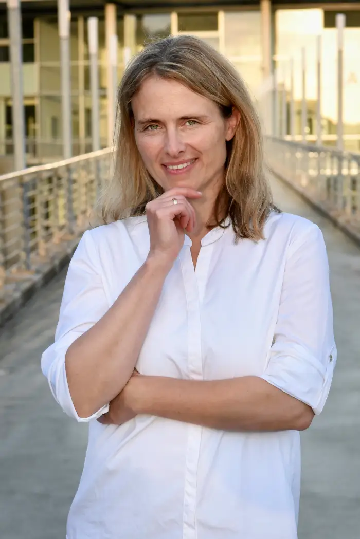 Nicole Tepaße von Rede Klartext steht vor einem modernen Gebäude, lächelt in die Kamera und präsentiert sich als Coachin für Kommunikation und Deeskalation